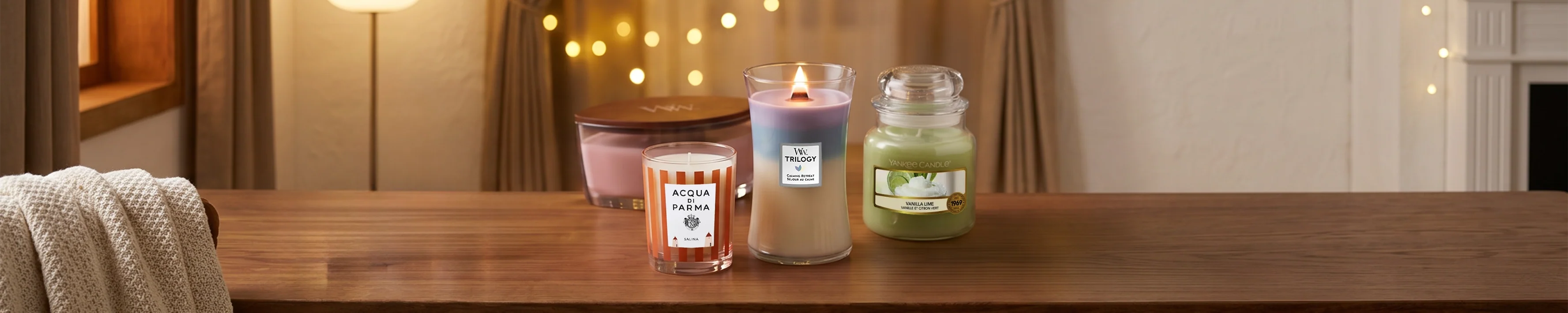Three luxury scented candles in jars on pink geometric pedestals with a minimal vase
