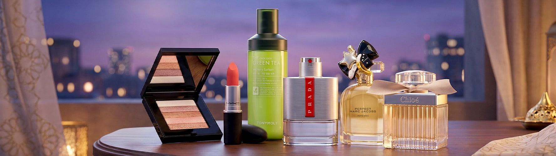 Luxury perfumes, skincare lotion, makeup palette, and lipstick on a table with city lights.