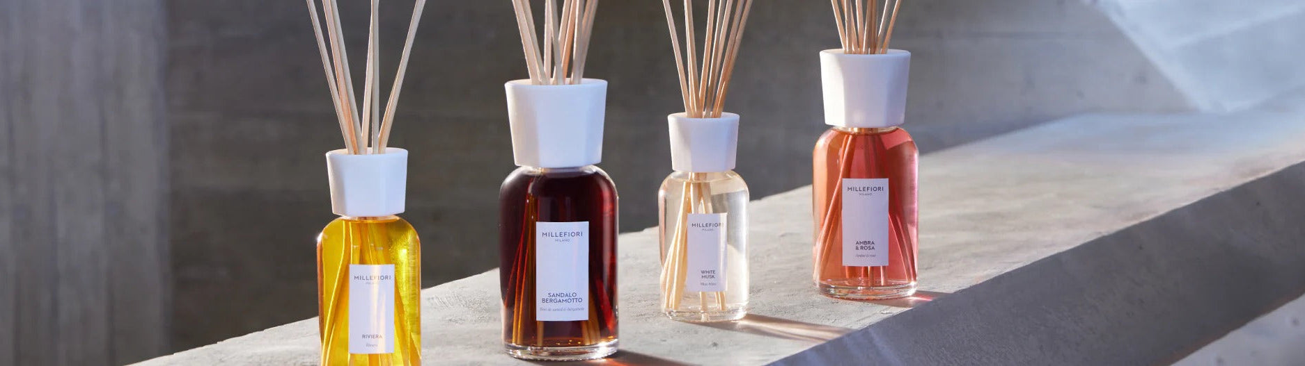 Four fragrance diffuser bottles with white caps and reed sticks on a stone surface
