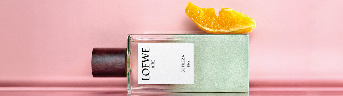 Five LOEWE Elixir perfume bottles with gradient colors and wooden caps, lined up on a soft blue background.